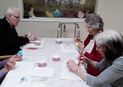 Residents at Lulworth House around a table painting Easter eggs and cups