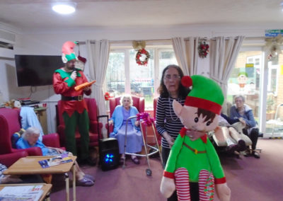 Residents at Lulworth House Residential Care Home in the lounge with festive elf costumes and large soft elf toy