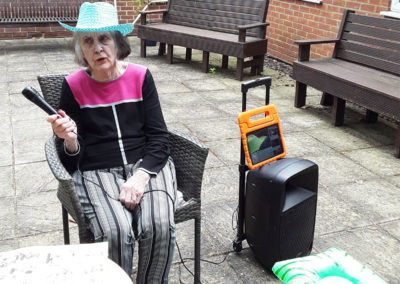 Lady resident sitting doing karaoke outside at Lulworth House Residential Care Home