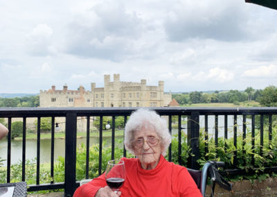 Lulworth lady resident outside with a glass of red wine with Leeds Castle in the distance behind her