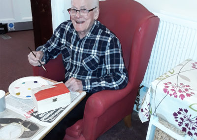 Gentleman resident painting a wooden treasure box with colourful paints at Lulworth House Residential Care Home