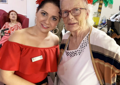 Staff member and resident posing for a photo wearing red and black Spanish style head garlands