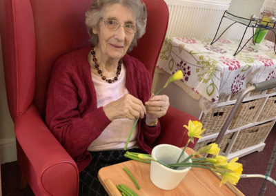 Female resident sitting in a chair arranging daffodils in a vase