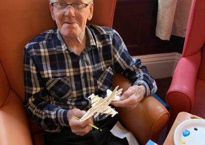 Male resident at Lulworth House Residential Care Home holding a small wooden model aeroplane he's made