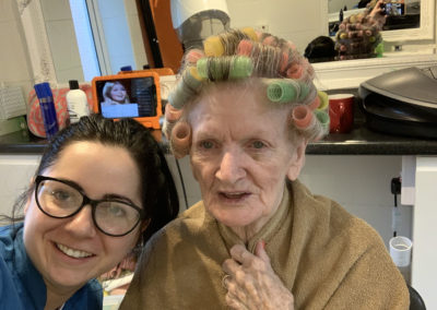 Lulworth House resident with her hair in rollers smiling at the camera with a staff member