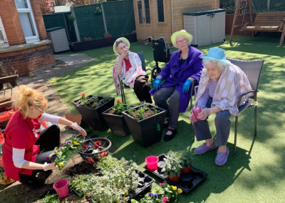 Ladies at Lulworth House Residential Care Home sitting in the garden while staff pot new colourful plants